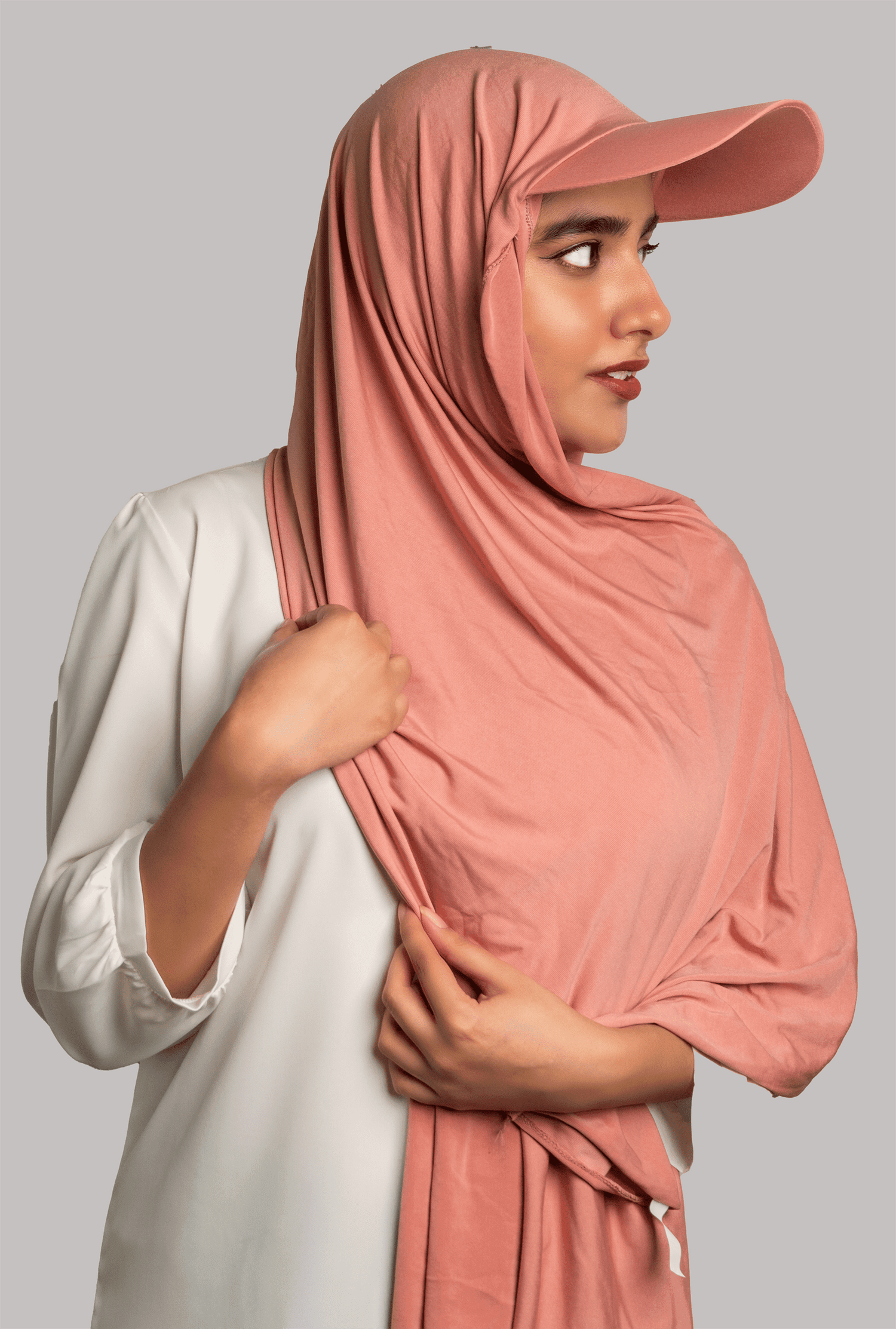 A women wearing a stylish Hat Hijab in pink color and a white top looking to her left