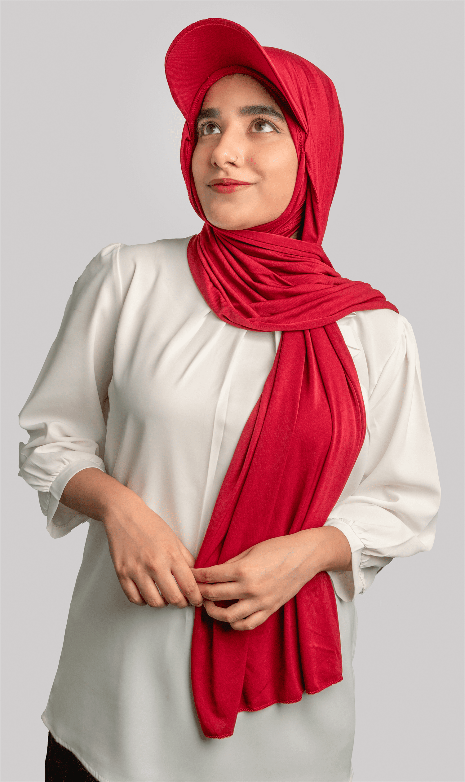 A women wearing a stylish Hat Hijab in maroon color and a white top looking to her right top of the corner