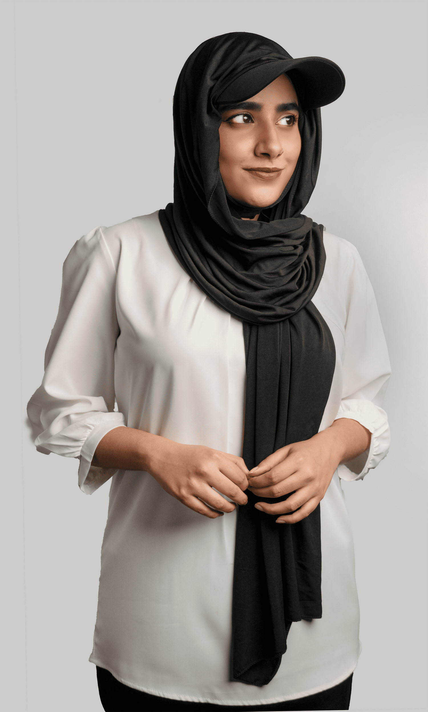 A women wearing a stylish Hat Hijab in black color and a white top looking to her left 