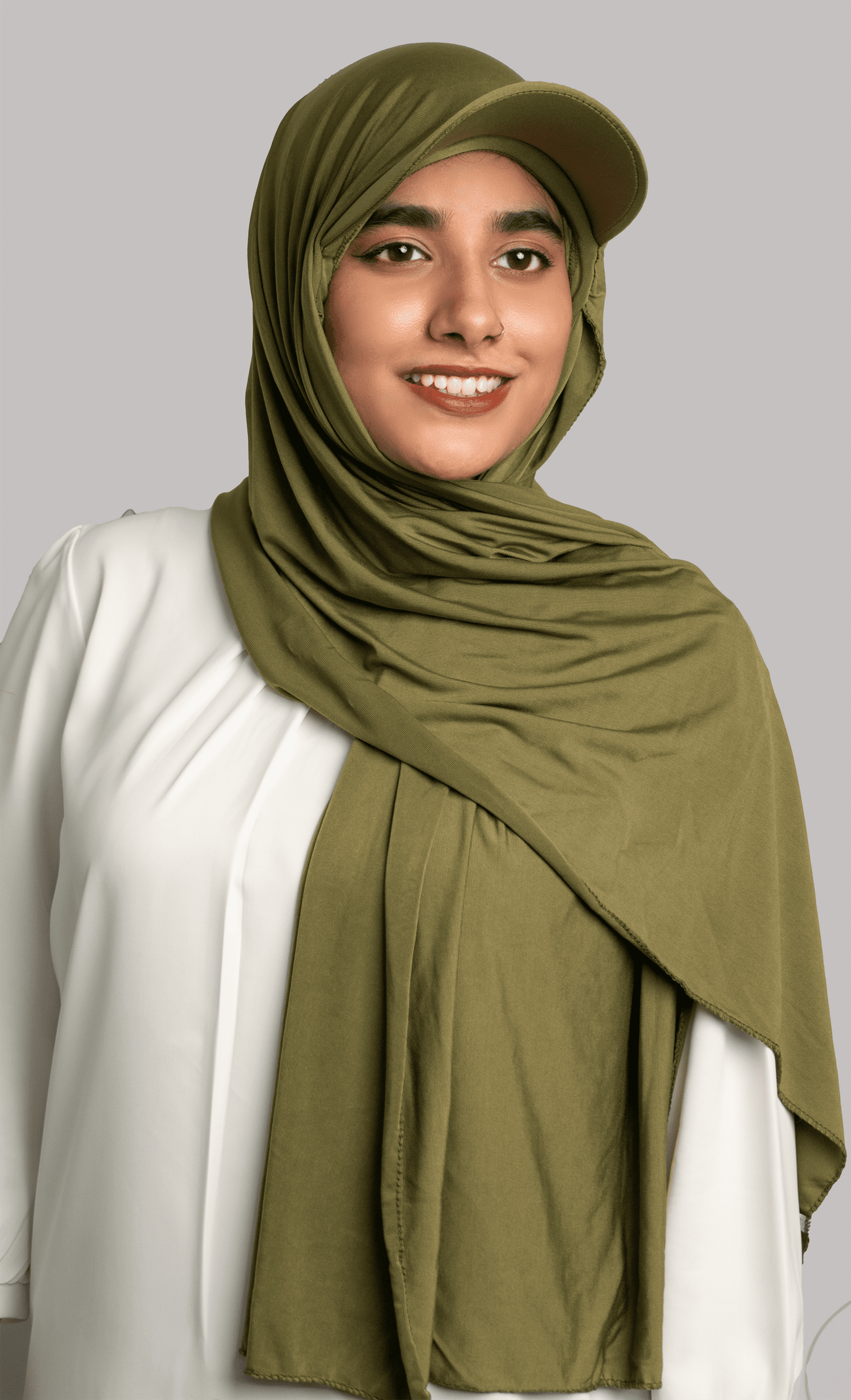 Woman wearing Hat Hijab in olive green over a white top looking to her straight. 