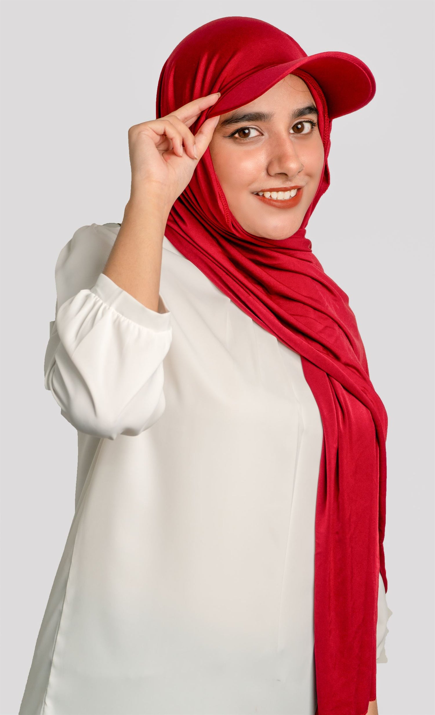 A girl wearing a stylish Hat Hijab in maroon color and a white top looking straight