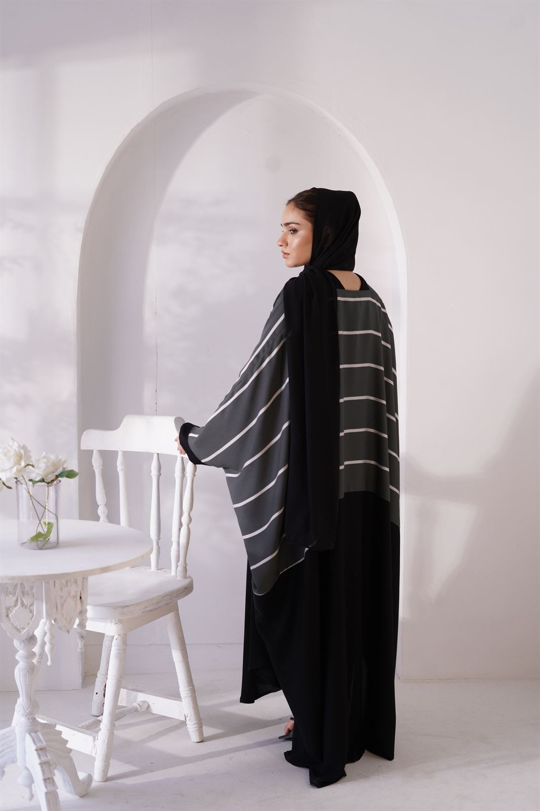 Back view of girl standing next to chair wearing zoom line abaya jilbab online.