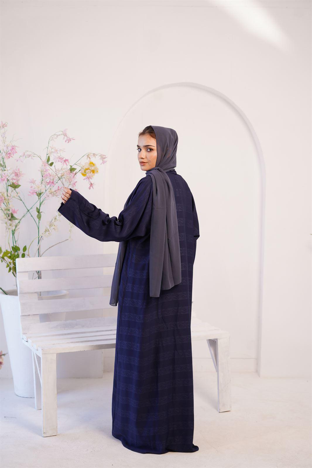 Girl Wearing Zoom Emboss navy blue Gown design abaya, standing beside a bench. back view. 