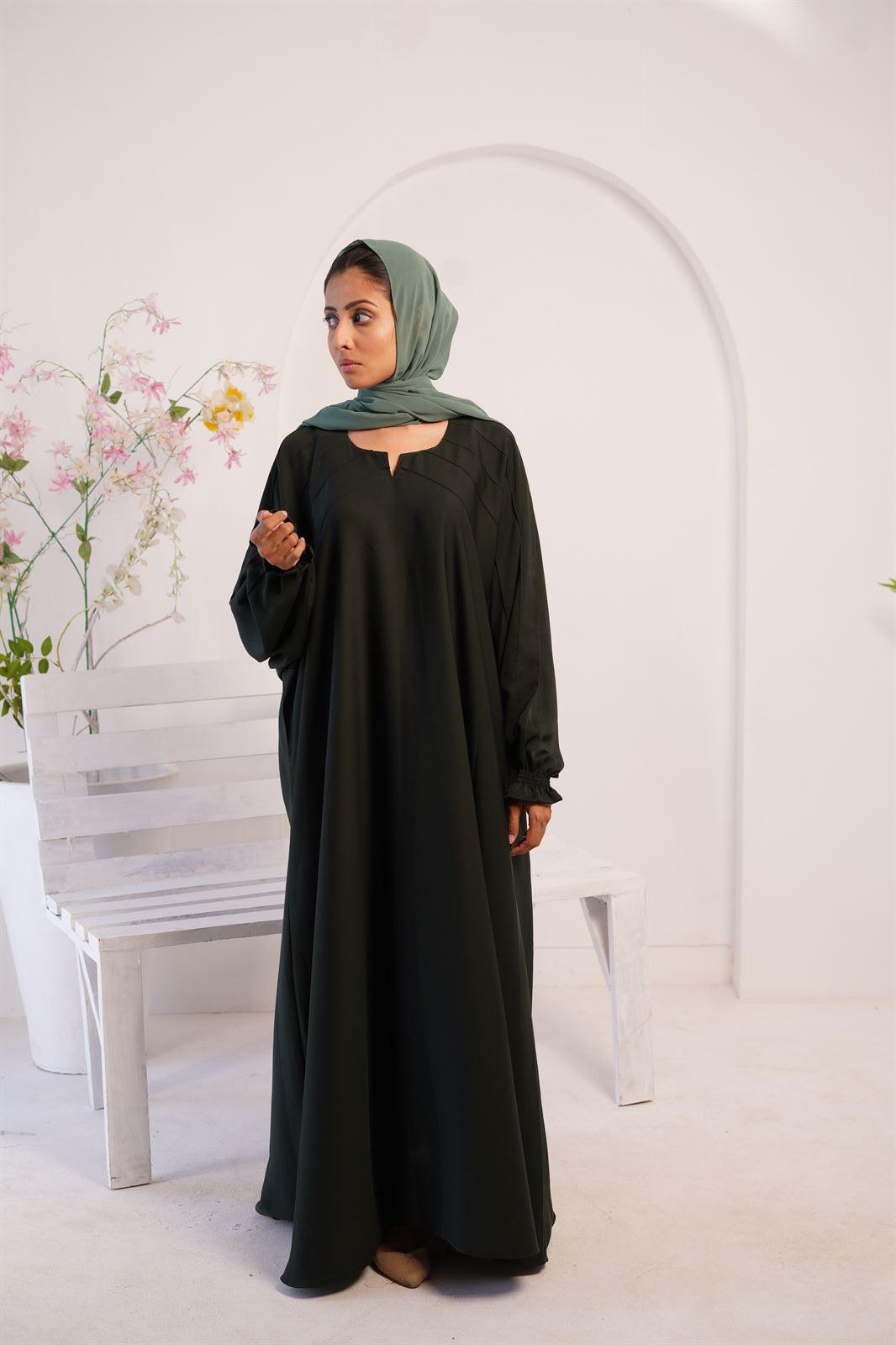 Buy Kaftan maxi abaya online in bottle green. Girl wearing it standing next to a bench.