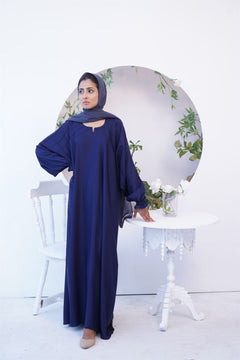 Girl wearing navy blue paintex kaftan maxi abaya burqa. Standing next to a chair.