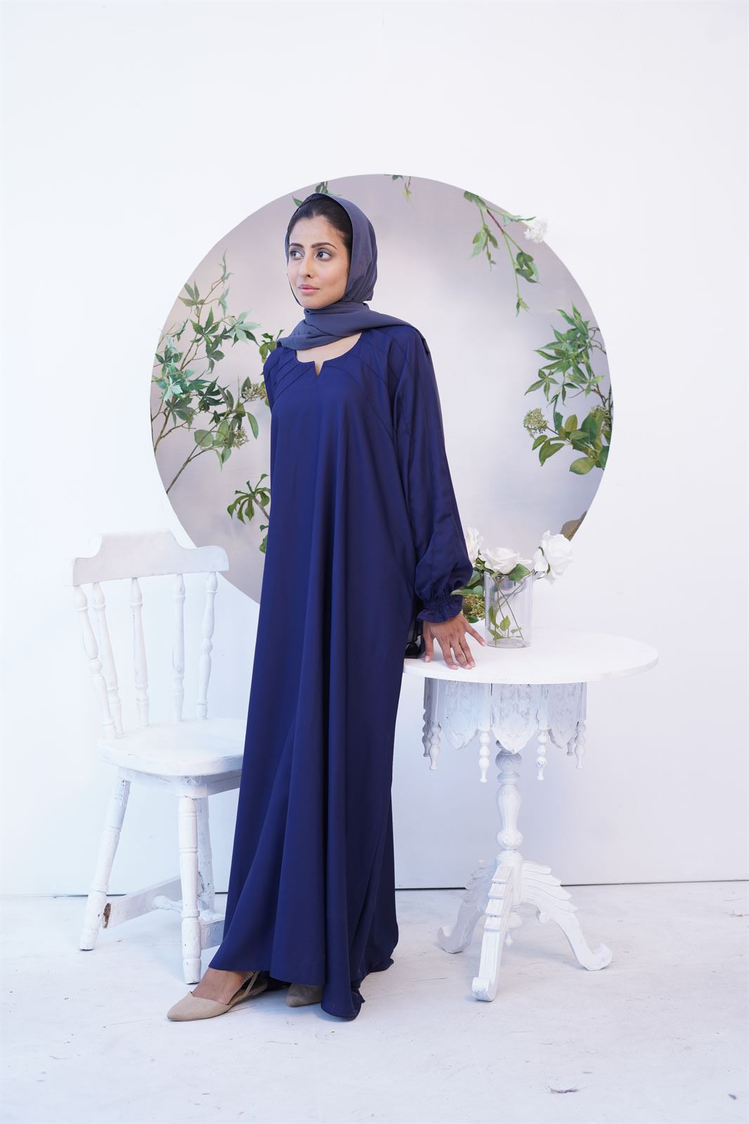 Girl wearing navy blue paintex kaftan maxi abaya burqa. Standing near table & chair.