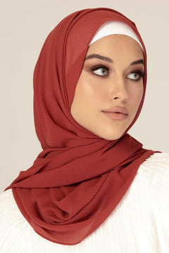 Georgette Hijab Online Pakistan, in brick color . a woman wearing it with white top looking her left.