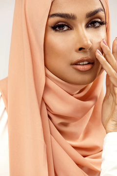 Georgette Hijab Online Pakistan, in creamy peach color. A woman wearing it with white top looking her straight.