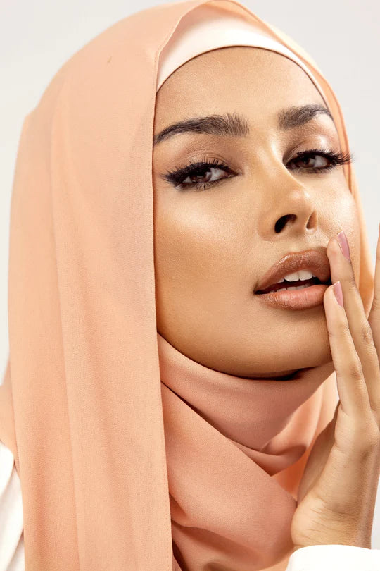 Georgette Hijab Online Pakistan, in creamy peach color. A woman wearing it with white top looking her straight.