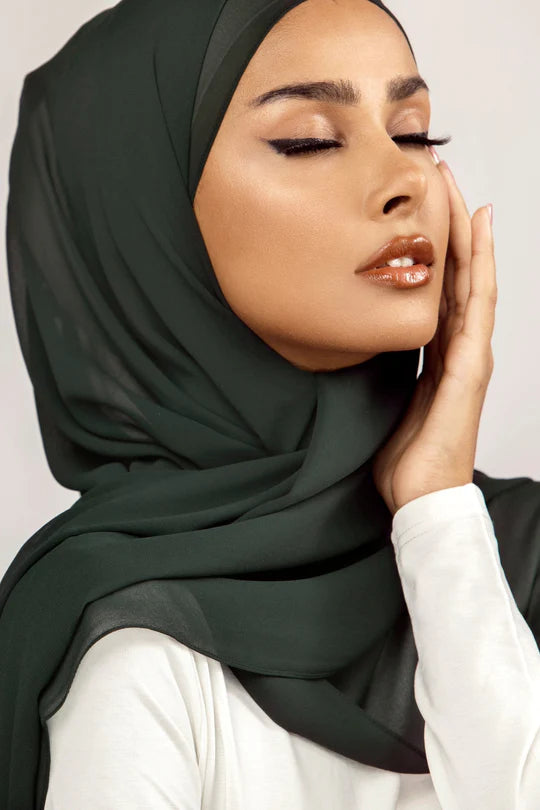 Georgette Hijab Online Pakistan, in bottle green color. A woman wearing it with white top looking her left.