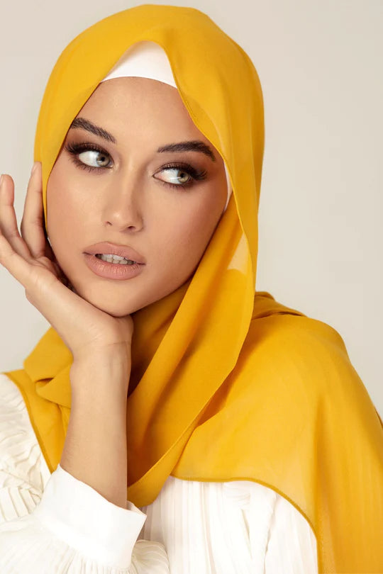 Georgette Hijab Online Pakistan, in mustard color. A woman wearing it with white top looking her left.