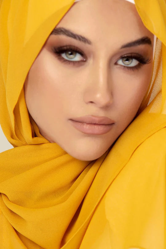 Georgette Hijab Online Pakistan, in mustard color. A woman wearing it with white top looking her straight.