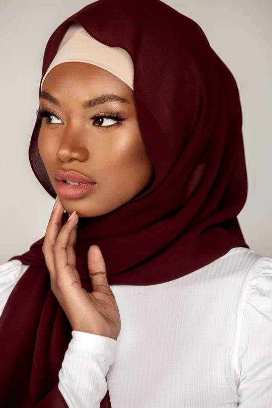 Georgette Hijab Online Pakistan, in mahogany color . a woman wearing it with white top looking her right.