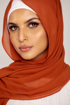 Georgette Hijab Online Pakistan, in burnt orange color. A woman wearing it with white top looking her straight.