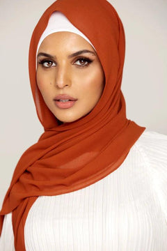 Georgette Hijab Online Pakistan, in burnt orange color. A woman wearing it with white top looking her straight.