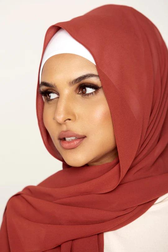 Georgette Hijab Online Pakistan, in rust color. A woman wearing it with white top looking her right.