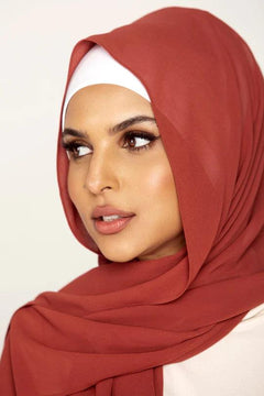 Georgette Hijab Online Pakistan, in rust color. A woman wearing it with white top looking her right.