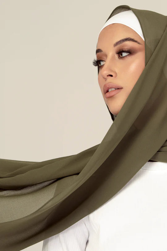 Hijab in sage color, stylish hijabi draping over white top looking her right.