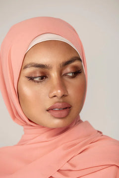 Georgette Hijab Online Pakistan, in soft peach color. A woman wearing it with white top looking her left.